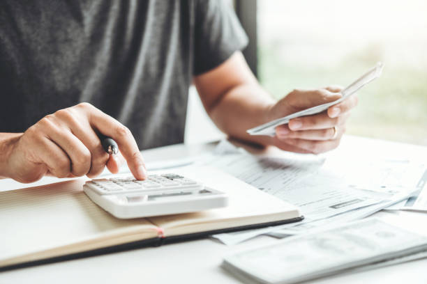 A person is using a calculator and holding a phone while working with documents.