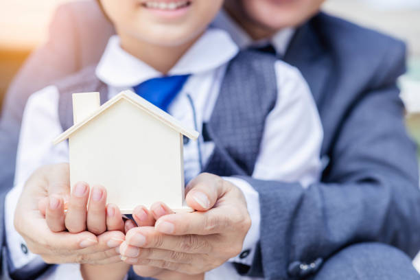 An adult in a suit and a child hold a small wooden house model together.